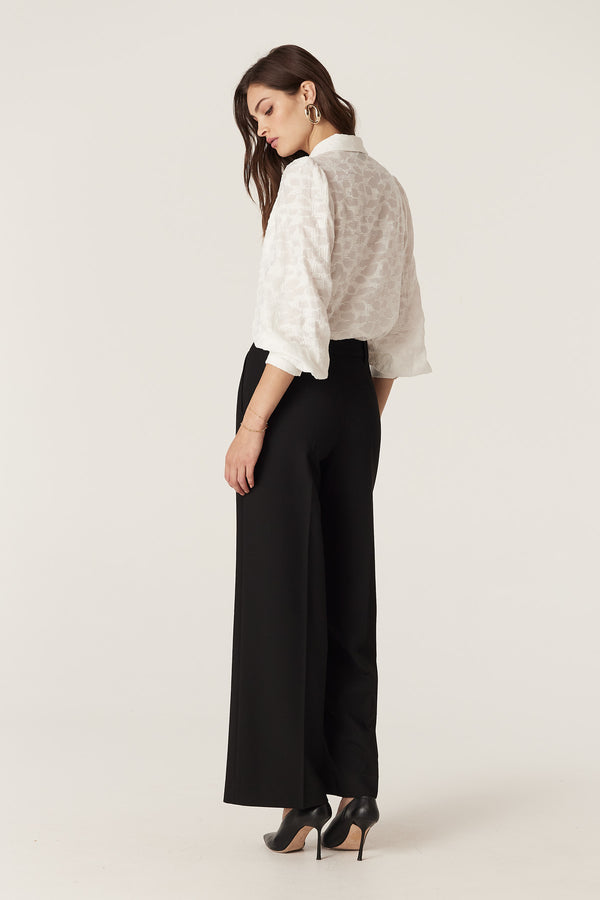 Model wearing an ecru Vella Jacquard Blouse with soft sleeve gathers and shell buttons, paired with black trousers.