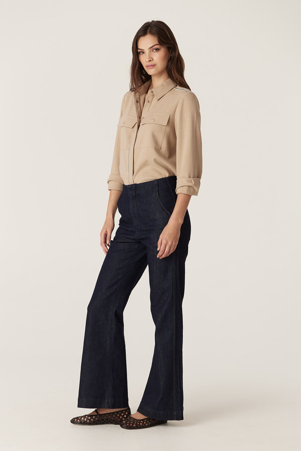 Woman wearing a camel Row Shirt with gold snaps and braid trim, paired with dark denim pants.