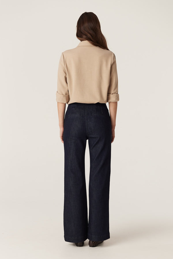 Woman wearing a camel Row Shirt with rolled sleeves, gold snaps, and dark wide-leg pants.