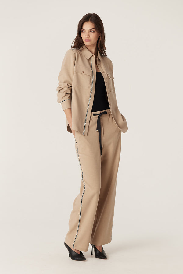 Woman in a camel Row Shirt and matching pants with black braid trim, gold snaps, and a black belt.