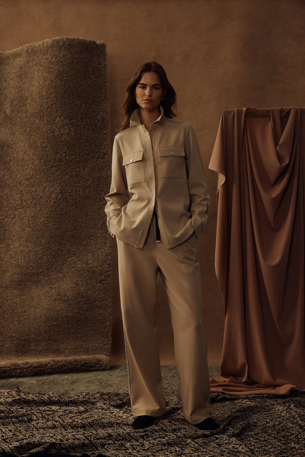 Woman in camel Row Pant and matching shirt with contrast braid trim, elasticated waist, and side pockets.