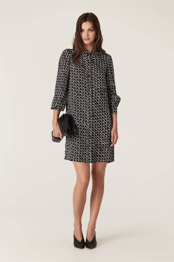 Woman in a black and white geo print Hamilton dress, silk blend, with a shirt collar and shirred cuffs.