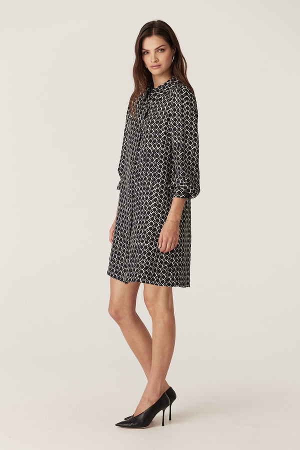 Model wears a black geo print Hamilton dress with shirred cuffs and a shirt collar, made from a silk blend twill.
