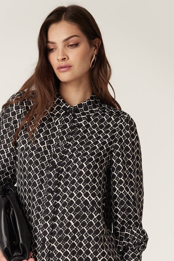 Woman in a black and white geo print Hamilton dress, featuring a shirt collar, button front, and shirred cuffs.