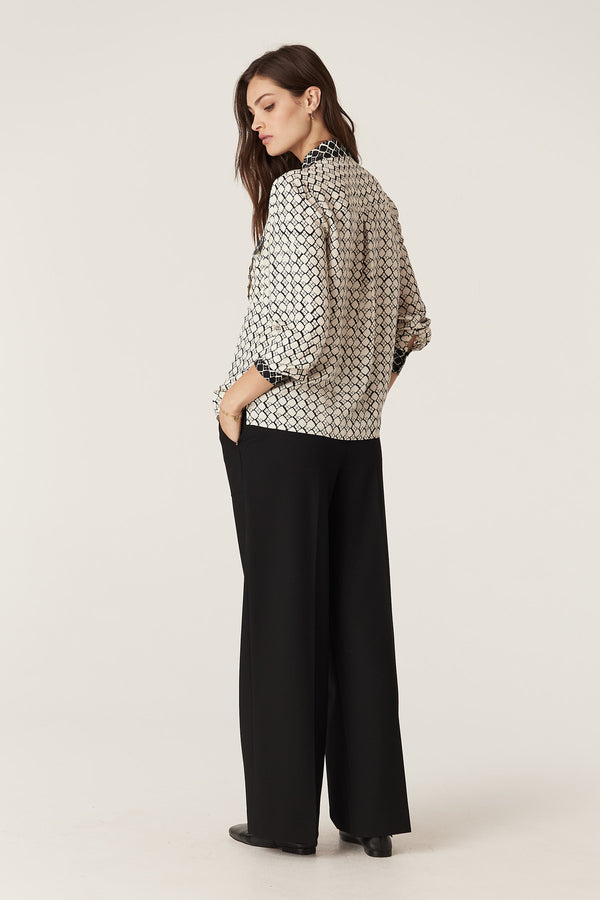 Hamilton Blouse in ivory geo print silk blend, with black cuffs and collar, paired with black pants.