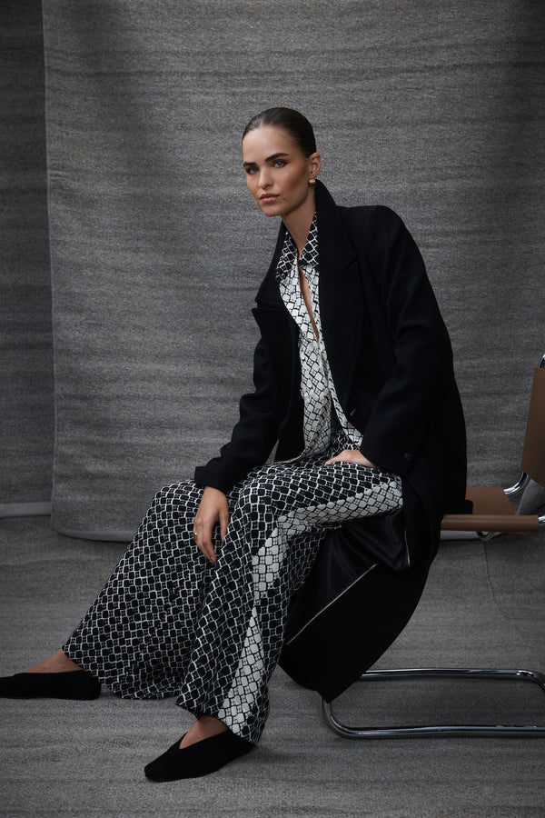 Model in black geo print silk blend Hamilton Pant with wide leg, black coat, and matching blouse.