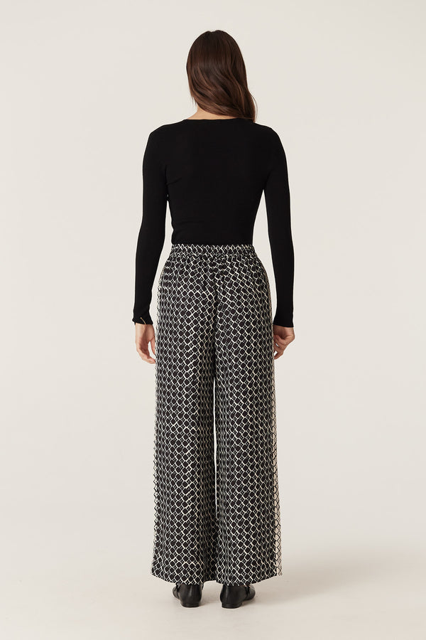 Woman from behind wearing black geo print wide-leg Hamilton silk blend pants with a black top.