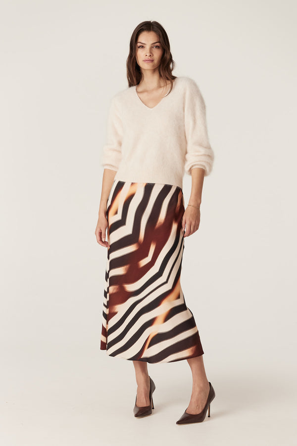 Woman in a bias-cut Sasha Zebra print midi skirt with a subtle sheen, paired with a cream sweater.
