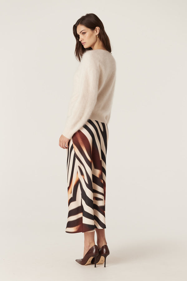 Woman in a bias-cut Sasha Zebra Print skirt, black and brown, with a cream sweater and heels.