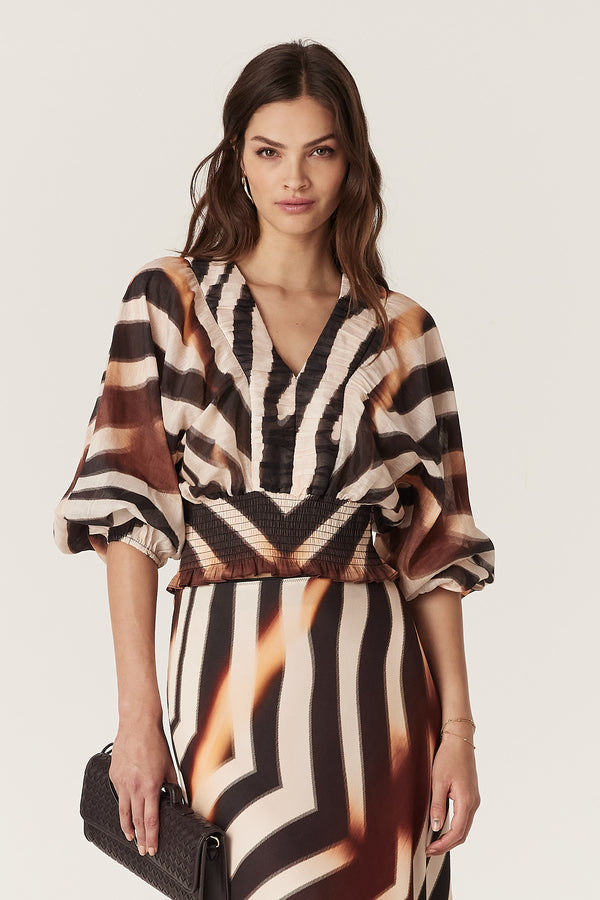Woman wearing a Sasha Blouse with brown and black zebra print, V-neck, batwing sleeves, and shirred waist.