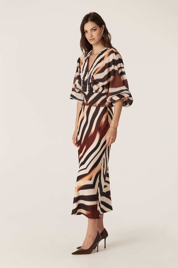 Woman wearing a Sasha Blouse in zebra print with a V-neck, ruched detail, batwing sleeves, and shirred waist.