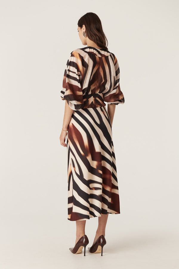 Woman in a relaxed fit Sasha Blouse with brown and black zebra print, V-neck, batwing sleeves, and shirred waist.