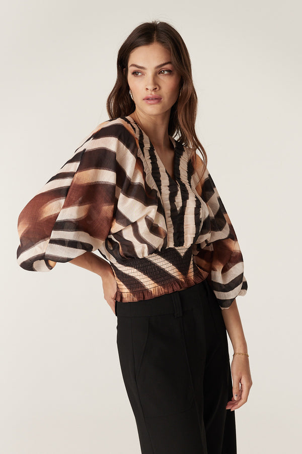 Model wears a relaxed fit Sasha Blouse in zebra print linen viscose with V-neck, ruched detail, and shirred waist.