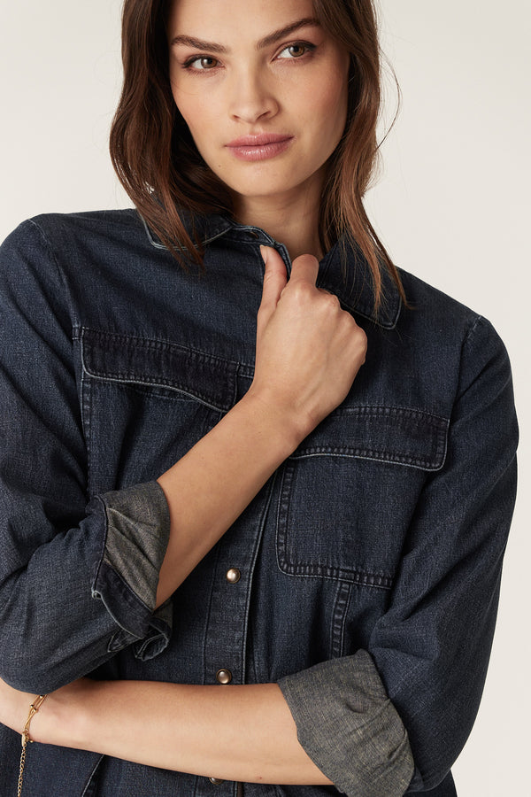 Woman wearing an indigo Dallas denim shirt with patch pockets, rolled sleeves, and cream press studs.
