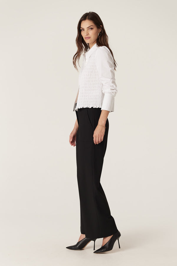 Woman wearing black Evie wide-leg pants with a high waistband, front patch pockets, and a white shirt.