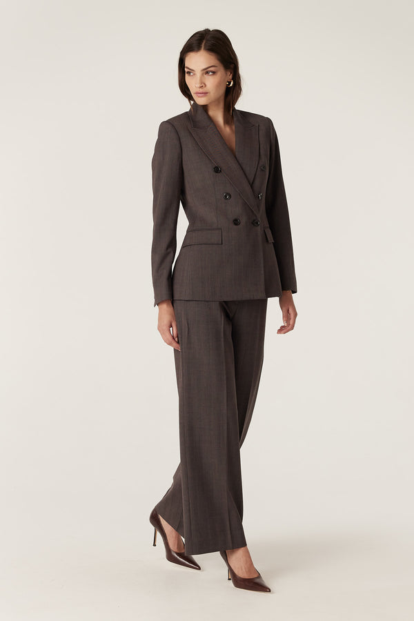 Woman in a mocha double-breasted wool blazer and matching pants with a subtle herringbone weave.