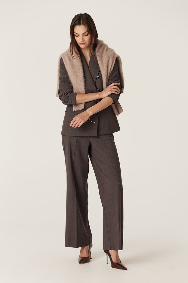 Woman in a mocha wool blend double-breasted blazer and matching pants, with a beige sweater draped over shoulders.