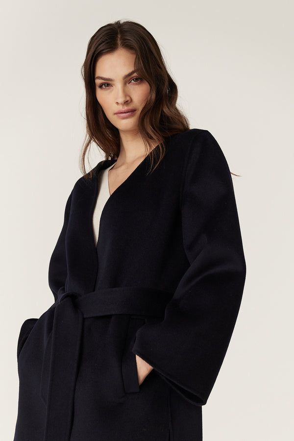 Woman in a navy Lawson wool coat with a relaxed fit, flared sleeves, and matching fabric belt.