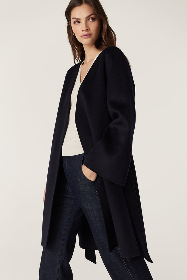 Woman wearing a navy Lawson Coat with relaxed fit, flared sleeves, and high-low hem, made from luxurious wool.