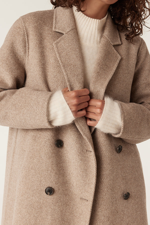 Close-up of a woman wearing a fawn Ainsley wool coat with a herringbone pattern and double-breasted buttons.