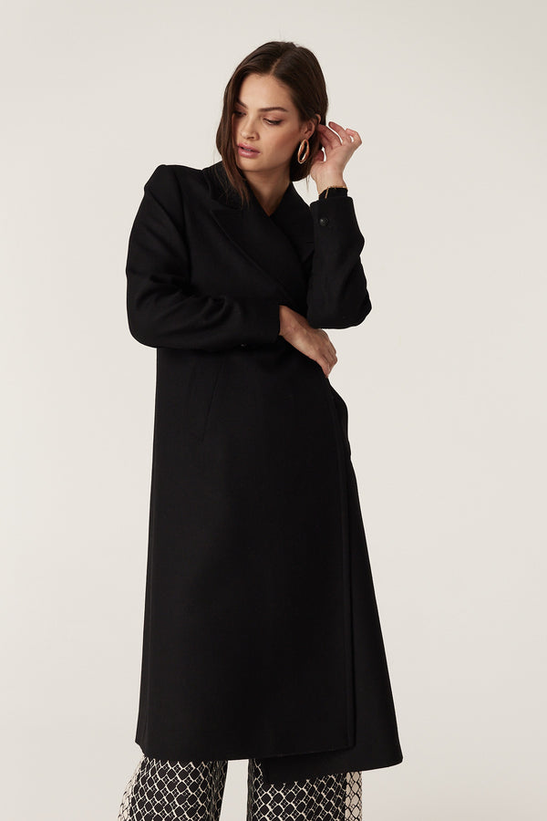 Woman in a black wool twill Montgomery coat with revere collar, double-breasted front, and pick stitch detail.