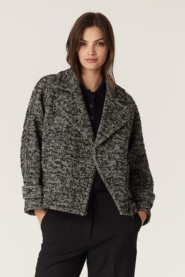 Woman wearing a black marle herringbone bouclé wool blend Roy Jacket with biker styling, black zip, and cuff tabs.