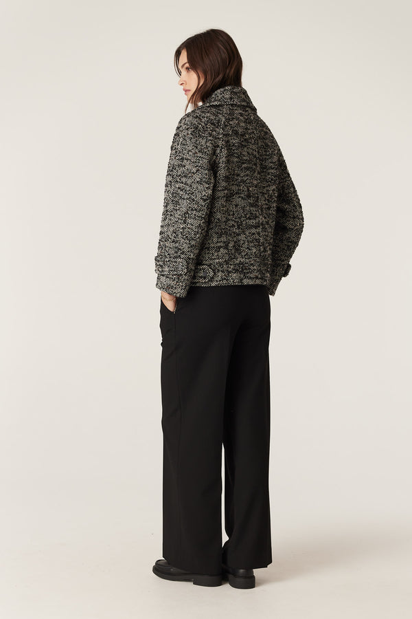 Woman in a black marle herringbone bouclé wool blend Roy Jacket with biker styling and black pants.