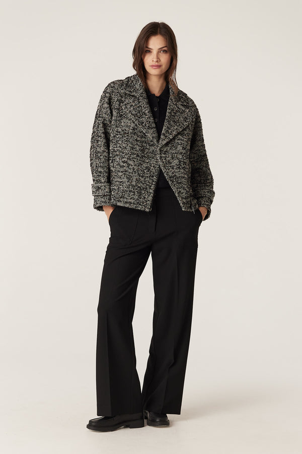 Woman wearing a relaxed fit black marle herringbone bouclé wool blend Roy Jacket with biker styling and black metal zip.