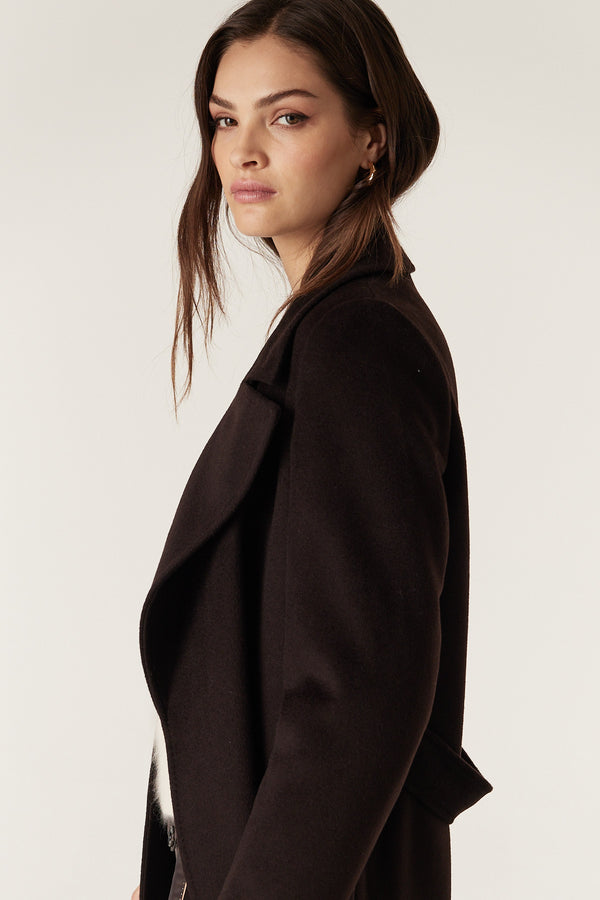 Woman wearing an Espresso Evans tailored wool coat with a wrap closure and pick stitch detail.