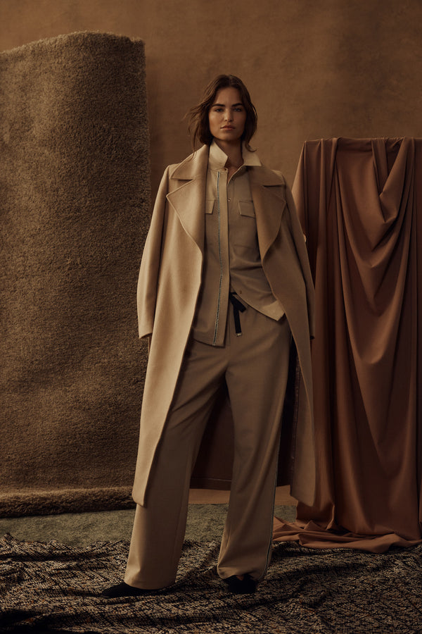 Woman in a tailored camel Evans wool coat with wrap closure, matching belt, and front pockets.