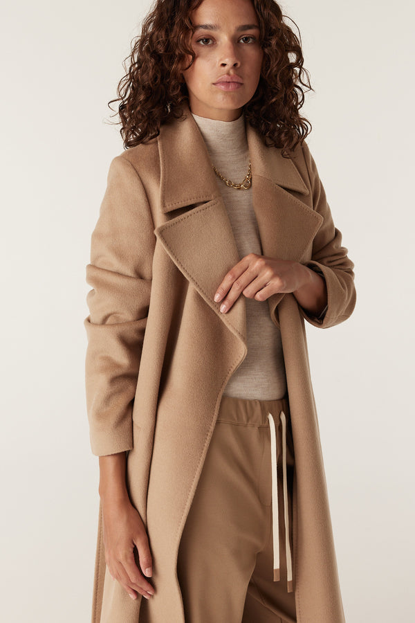 Woman in a camel Evans tailored wool coat with a wrap closure, matching belt, and front pockets.