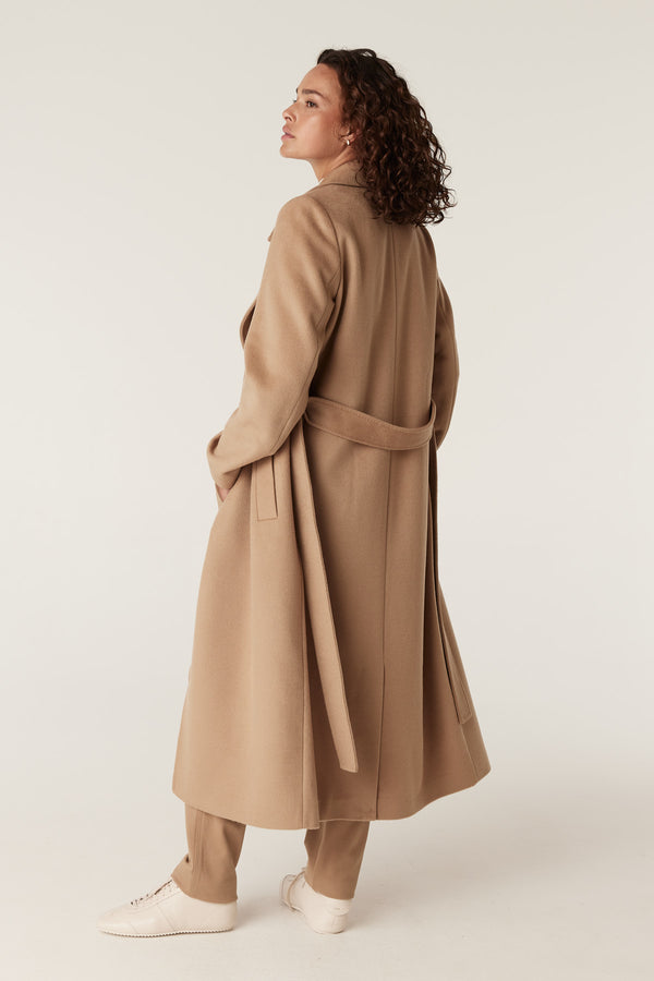 Woman in a camel Evans tailored wool coat with a wrap closure and matching fabric belt.