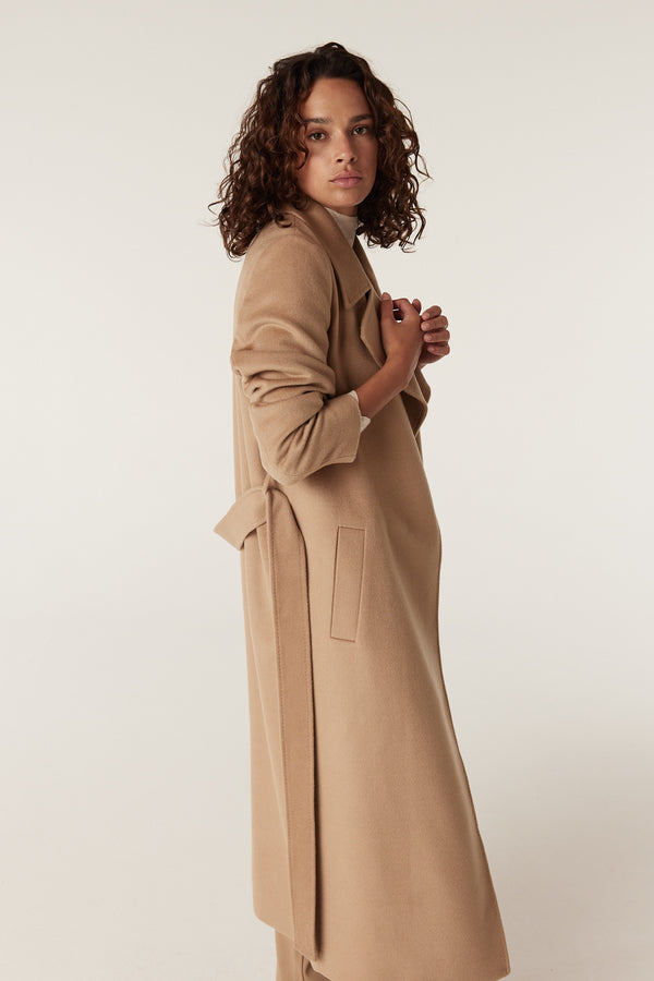 Woman in a camel Evans tailored wool coat with wrap closure, fabric belt, and front pockets.