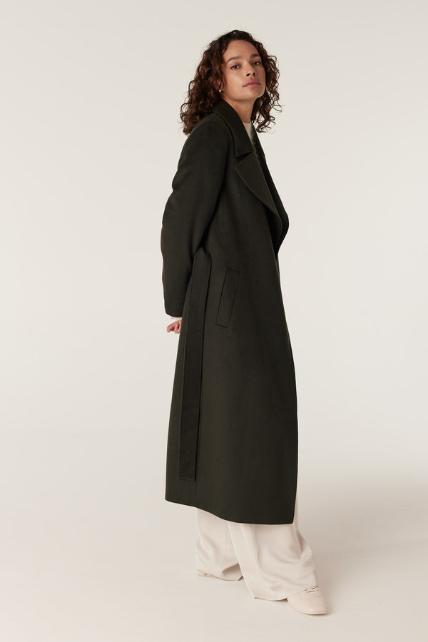 Model wearing a tailored forest green Evans wool coat with a wrap closure and fabric belt.