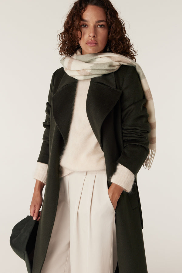 Woman in a forest green Evans wool coat, cream sweater, and plaid scarf.