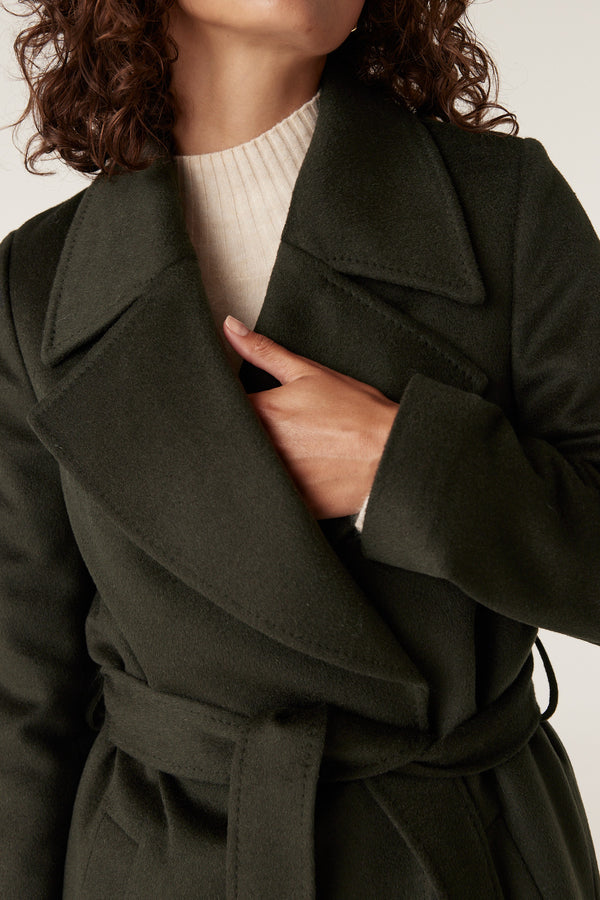 Close-up of a woman wearing a forest green Evans wool coat with a wrap closure and fabric belt.