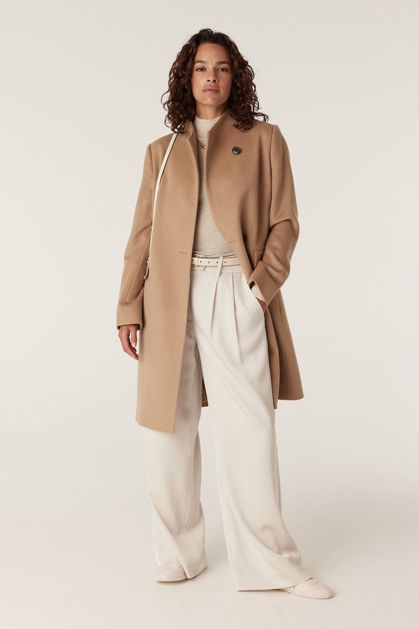 Woman modeling a camel Eton wool coat with a stand collar, single button closure, and side pockets.