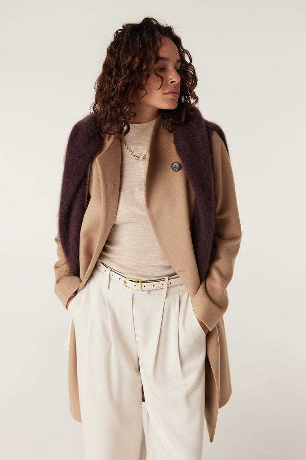 Camel Eton wool coat with a single button, worn over a cream turtleneck and pleated trousers.