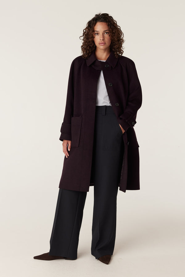 Woman wearing a dark port-colored Oxford coat with a classic collar, button front, and large pockets.