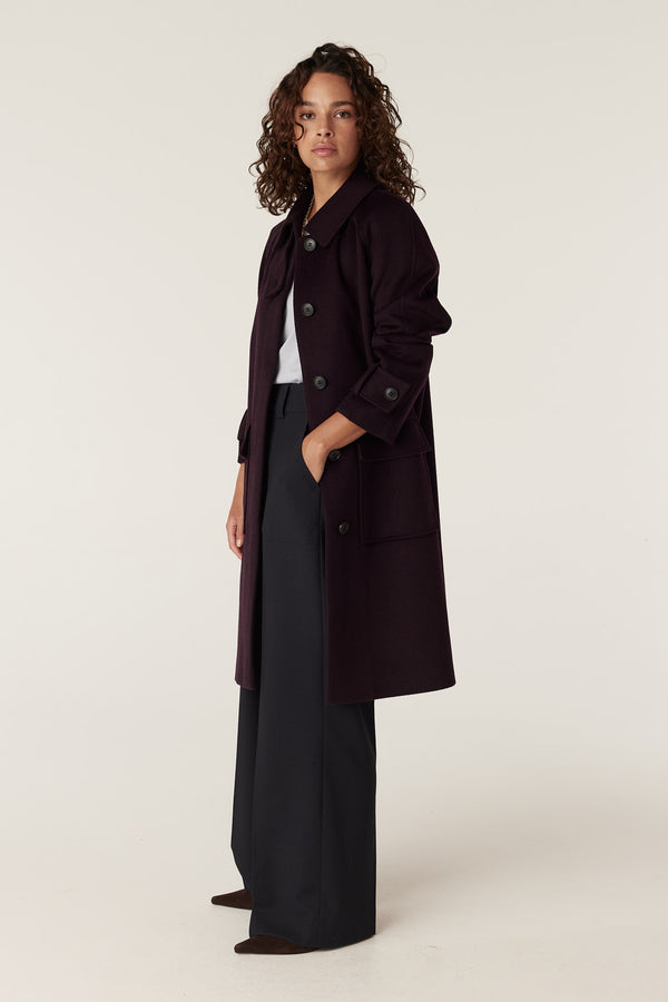 Woman wearing a port-colored Oxford wool coat with large buttons, wide lapels, and front pockets.