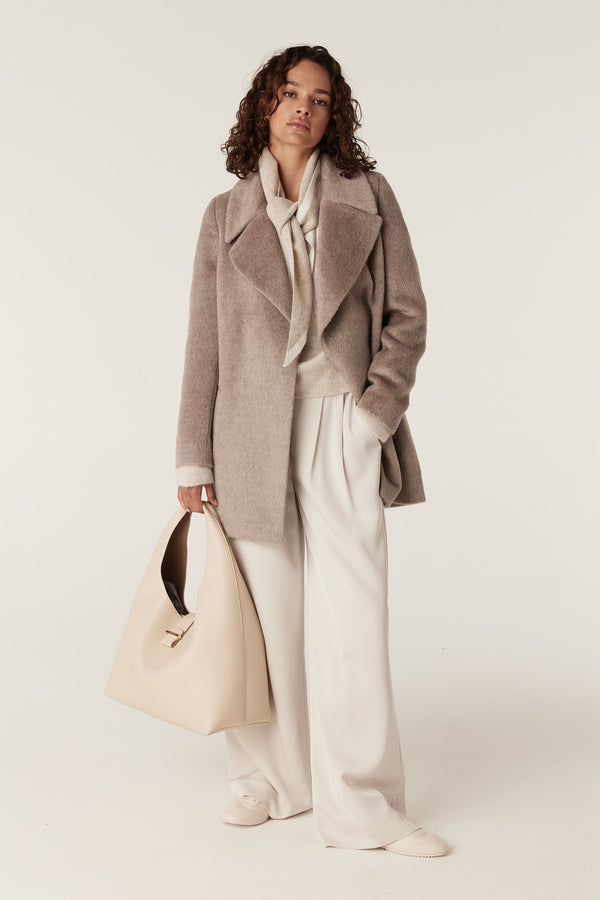 Woman in a fawn Sinclair wool coat, cream sweater, wide-leg trousers, and a large beige leather handbag.