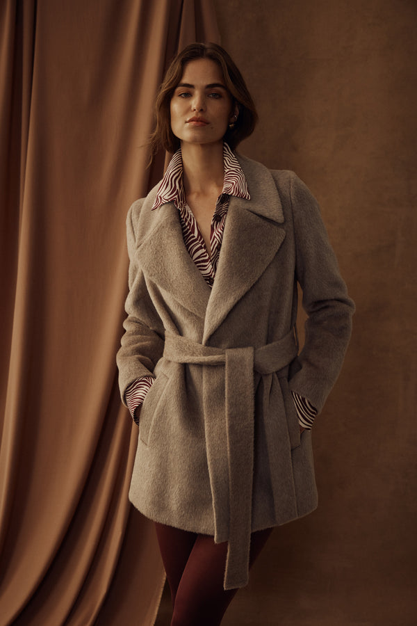 Woman in a fawn Sinclair wool coat with a belted waist, wide lapels, and a striped shirt.