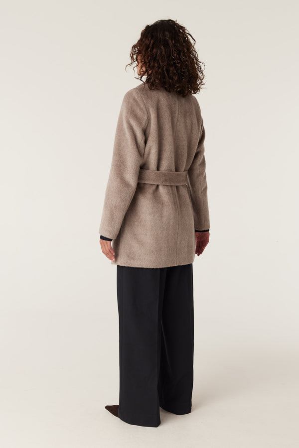 Woman from behind wearing a fawn Sinclair wool coat with a tie waist over dark pants.