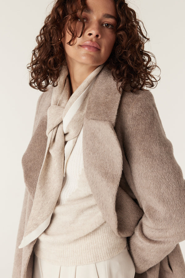 Woman in a fawn Sinclair coat, cream sweater, and striped scarf.