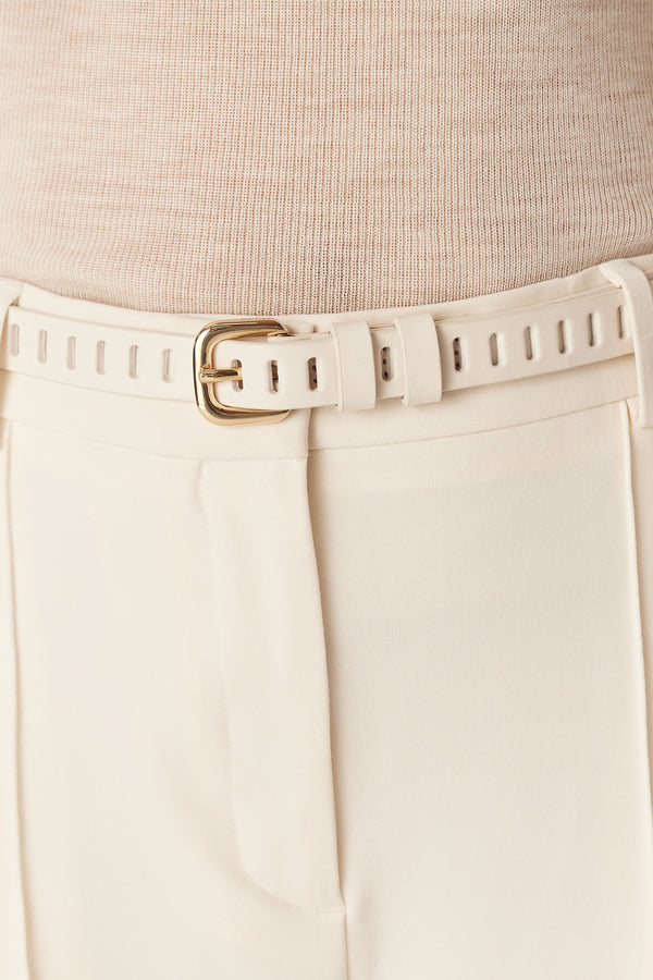 Ecru Fay leather belt with multiple eyelets and a gold buckle, worn with cream trousers.
