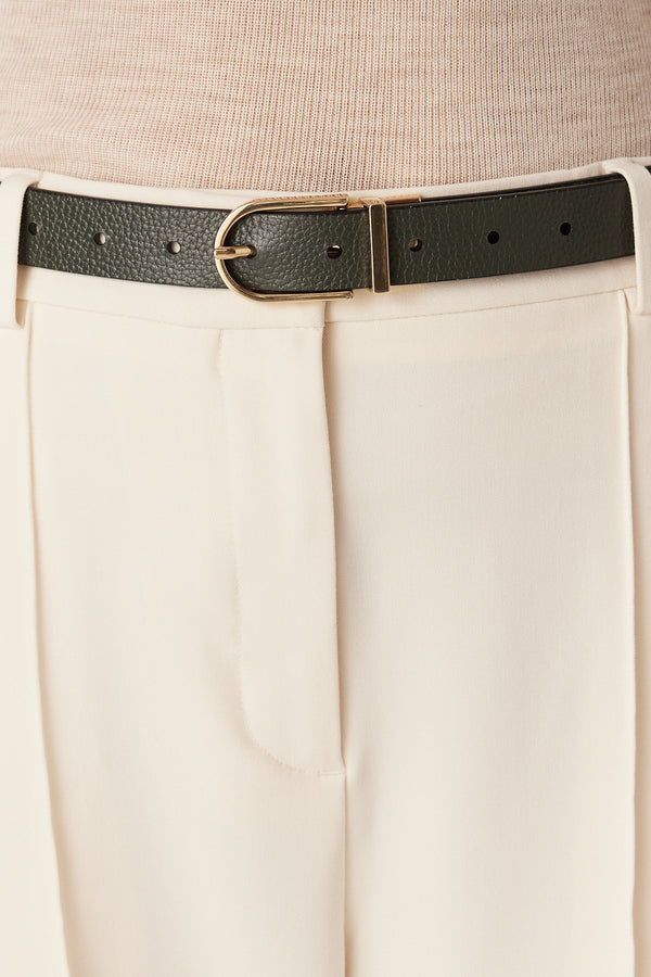 Reversible black and green genuine leather belt with a gold hardware buckle, worn with cream pants.