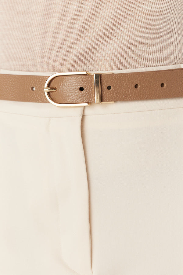 Tan genuine leather reversible belt with a gold buckle, worn with cream pants and a beige top.