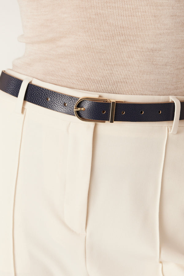 Navy genuine leather reversible belt with a gold buckle, worn with cream pants and a beige top.