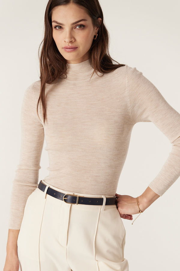 Woman wearing a slim navy genuine leather reversible belt with a gold buckle over cream pants and a beige top.