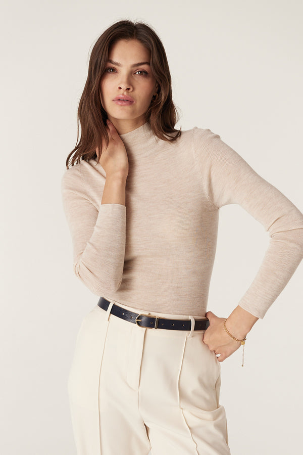 Woman wearing a navy genuine leather reversible belt with gold buckle, light beige turtleneck, and cream trousers.